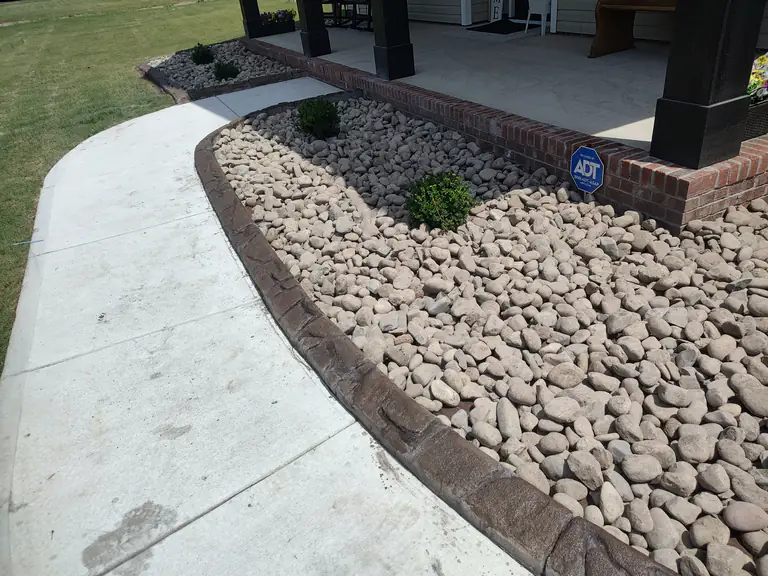 Close-up of curved concrete curbing along a rock-filled garden bed and walkway