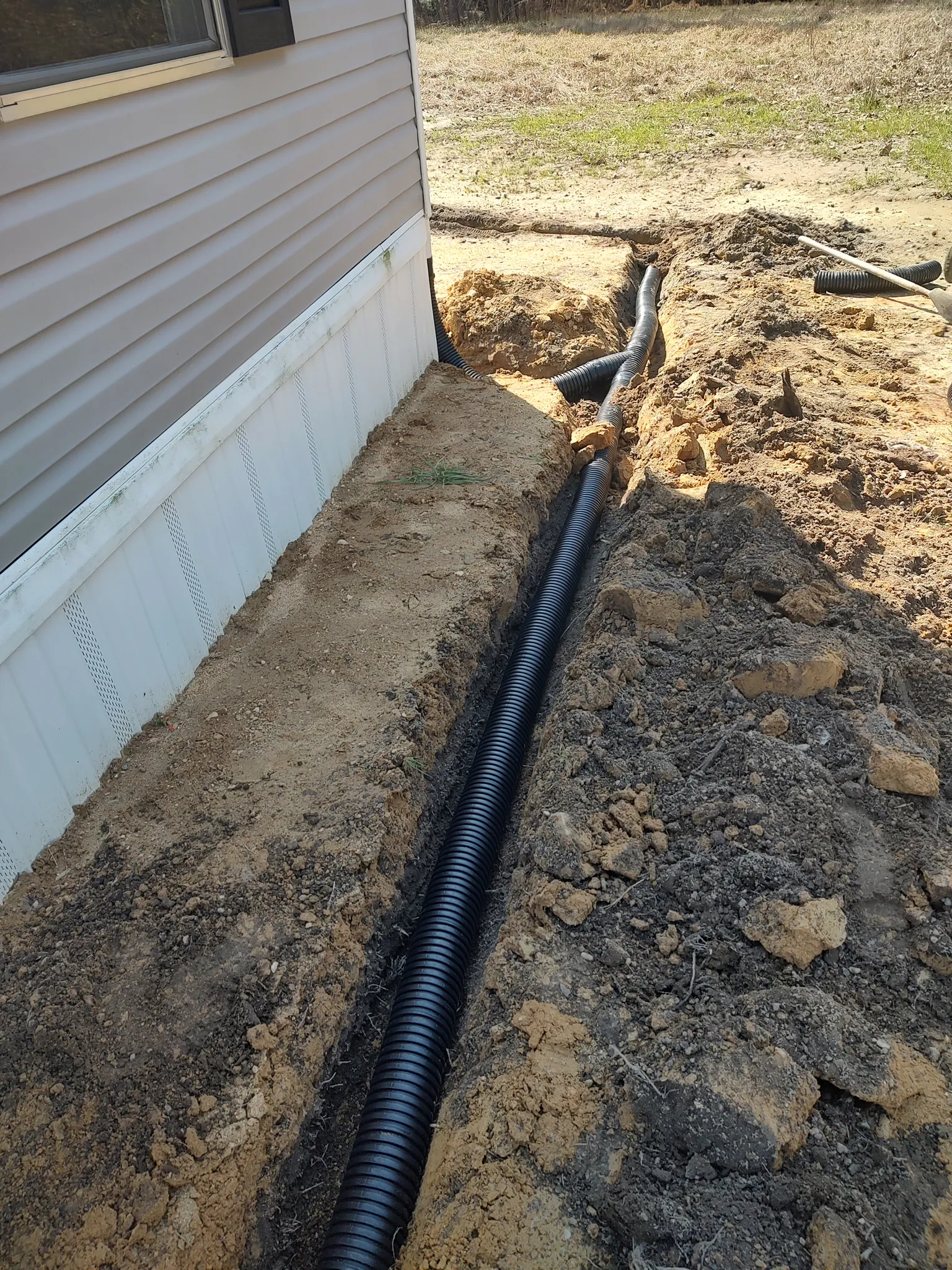 Perforated drain pipe laid in a long trench alongside a home before backfilling