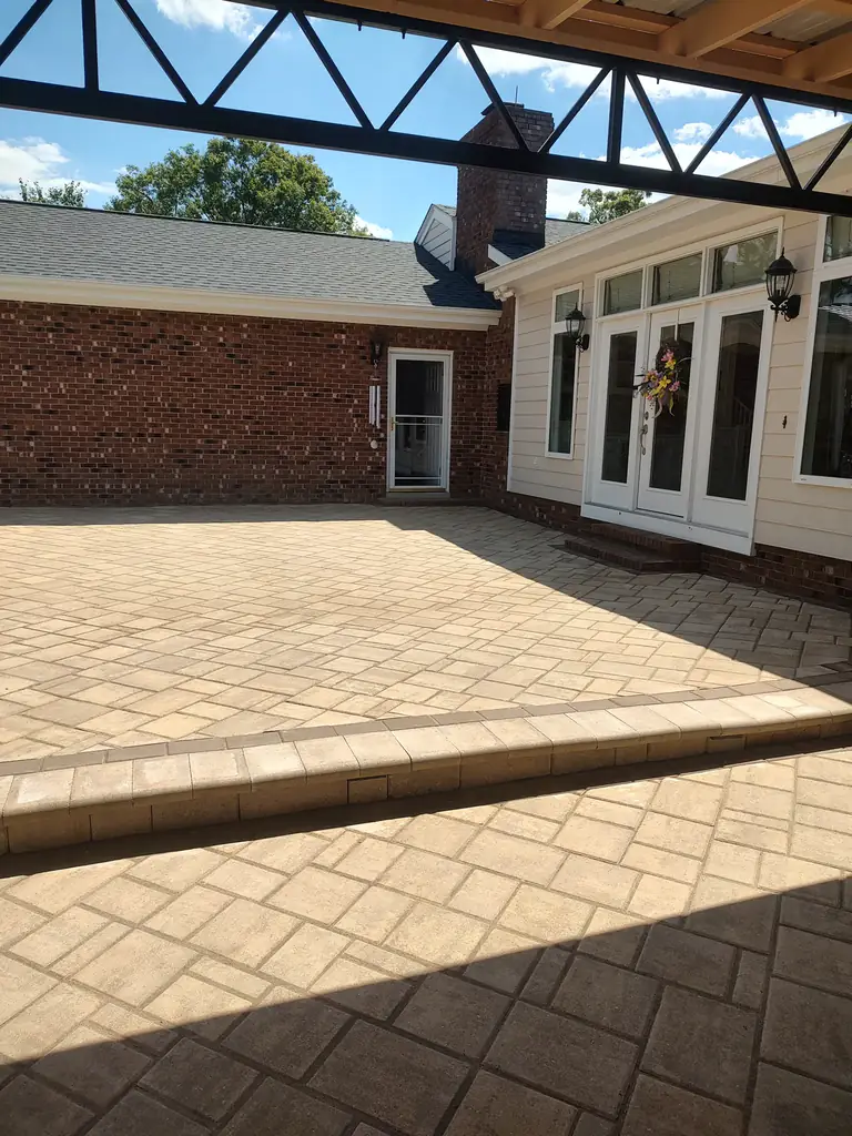 Sandstone paver patio under a covered structure beside a brick home