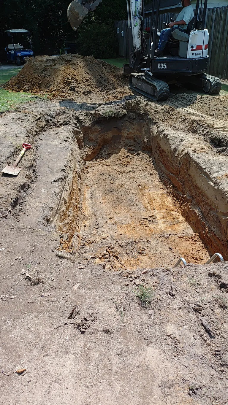 An excavated pond hole with shaped shelves dug into the yard before lining