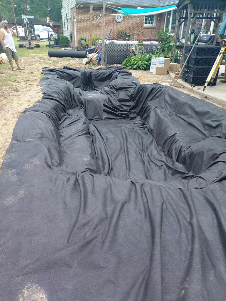 A koi pond excavation fitted with underlayment and a black EPDM pond liner