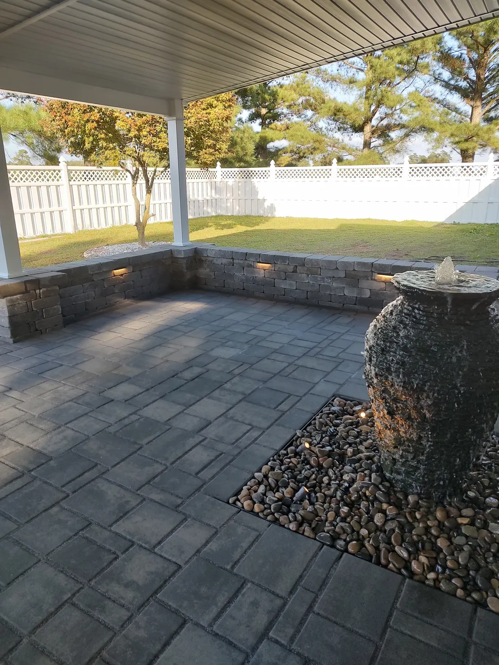 A finished backyard fountain surrounded by stone and plantings, built by Landscaping Plus LLC